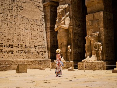 Closeup shot of a female standing in front of a Medinet Habu temple in Egypt