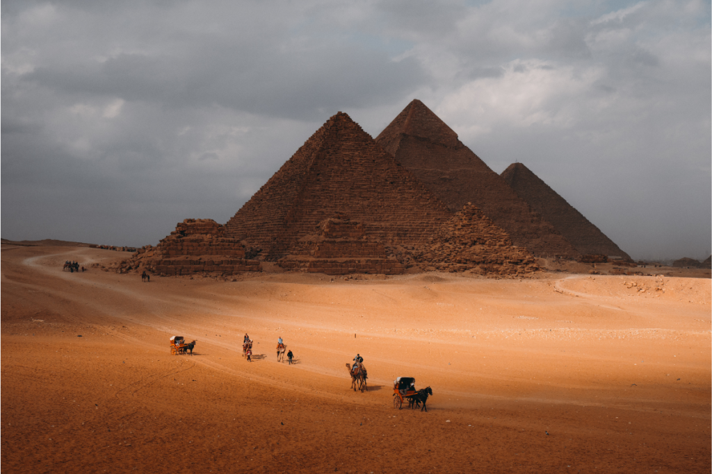 The Giza pyramids above the desert with camel riders crossing the sand