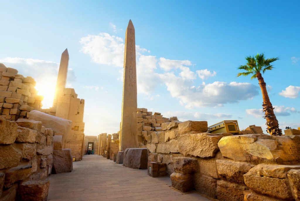 An obelisk and a palm tree above the stones of Karnak Temple