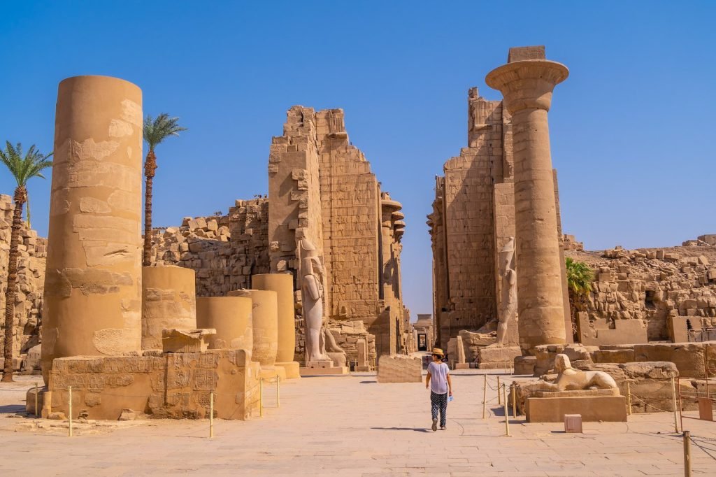 Columns and ruined gateways of Karnak Temple under a blue sky