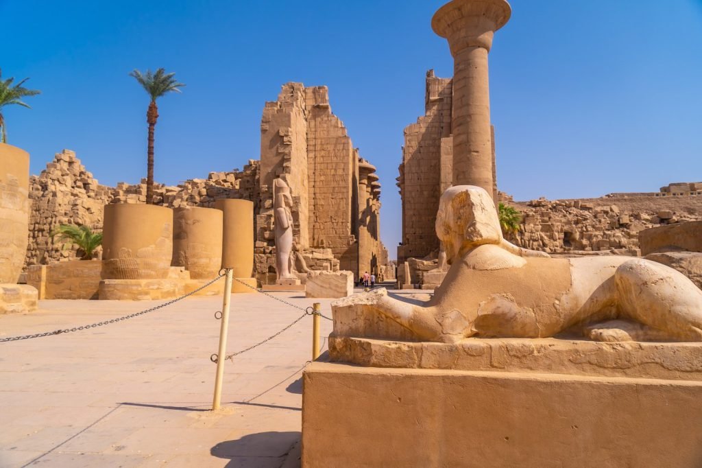 A sphinx statue in front of the ruined halls of Karnak