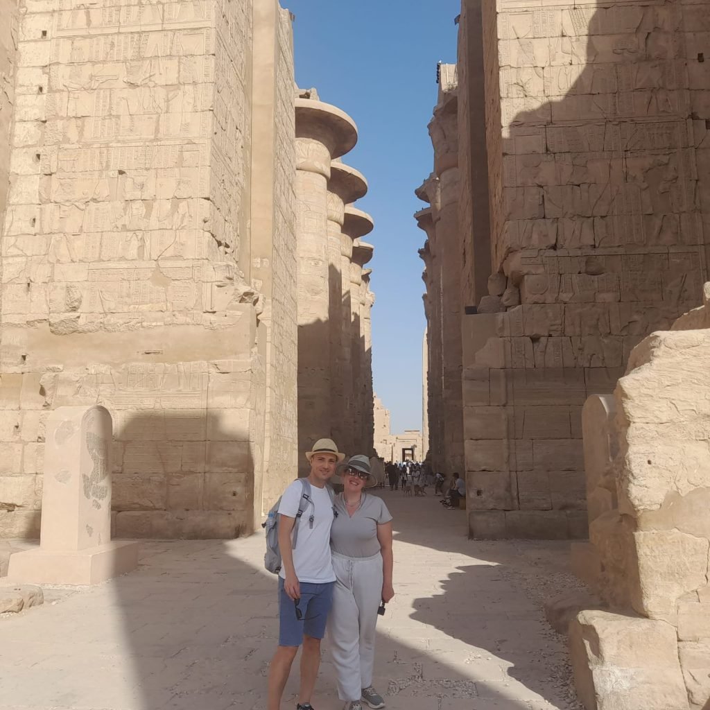Two travelers standing between the stone walls of Karnak Temple