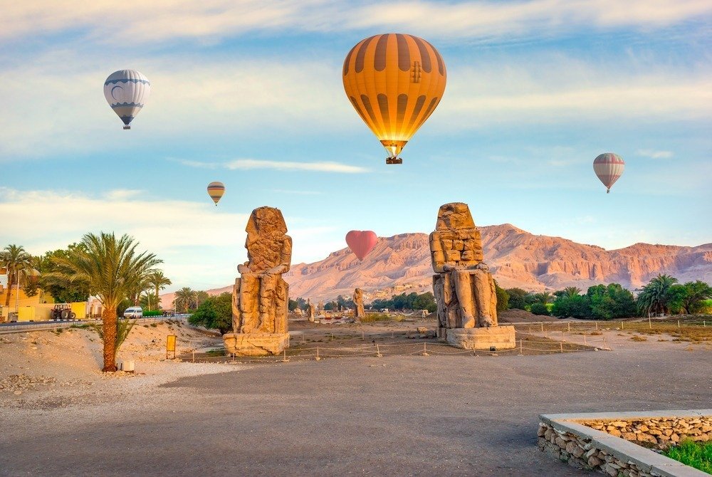 Hot air balloons rising over the Colossi of Memnon at sunrise