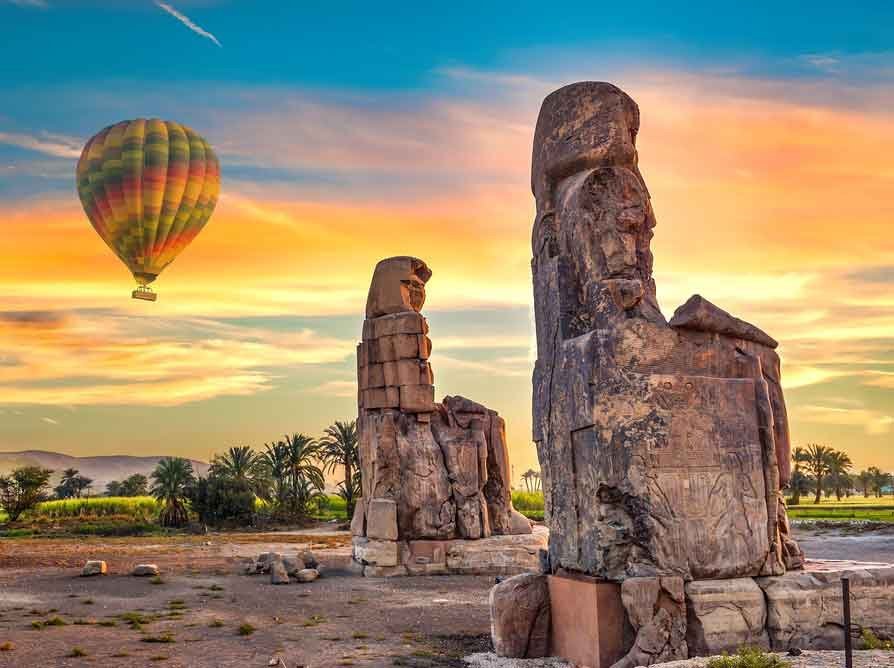 The Colossi of Memnon at sunrise with a hot air balloon in the sky
