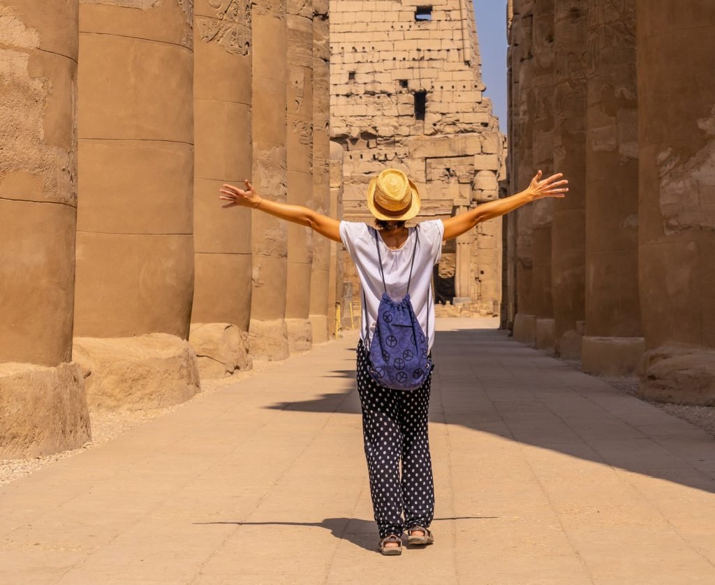 A traveler with arms raised in the colonnade of Luxor Temple