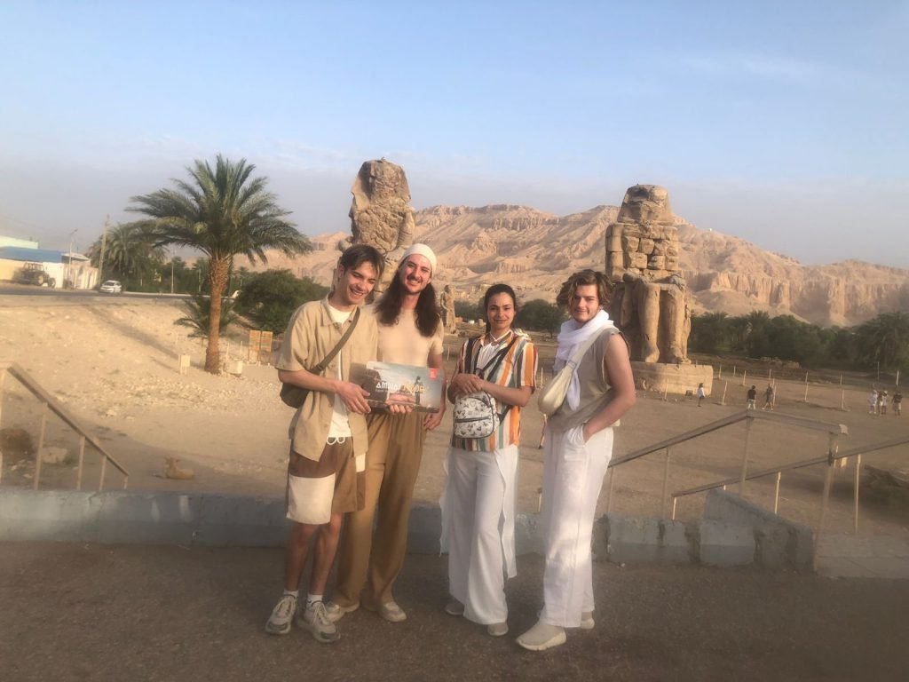 A group of travelers in early light with the Colossi of Memnon behind them