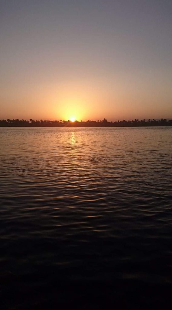 The sun setting over the Nile behind a line of palm trees