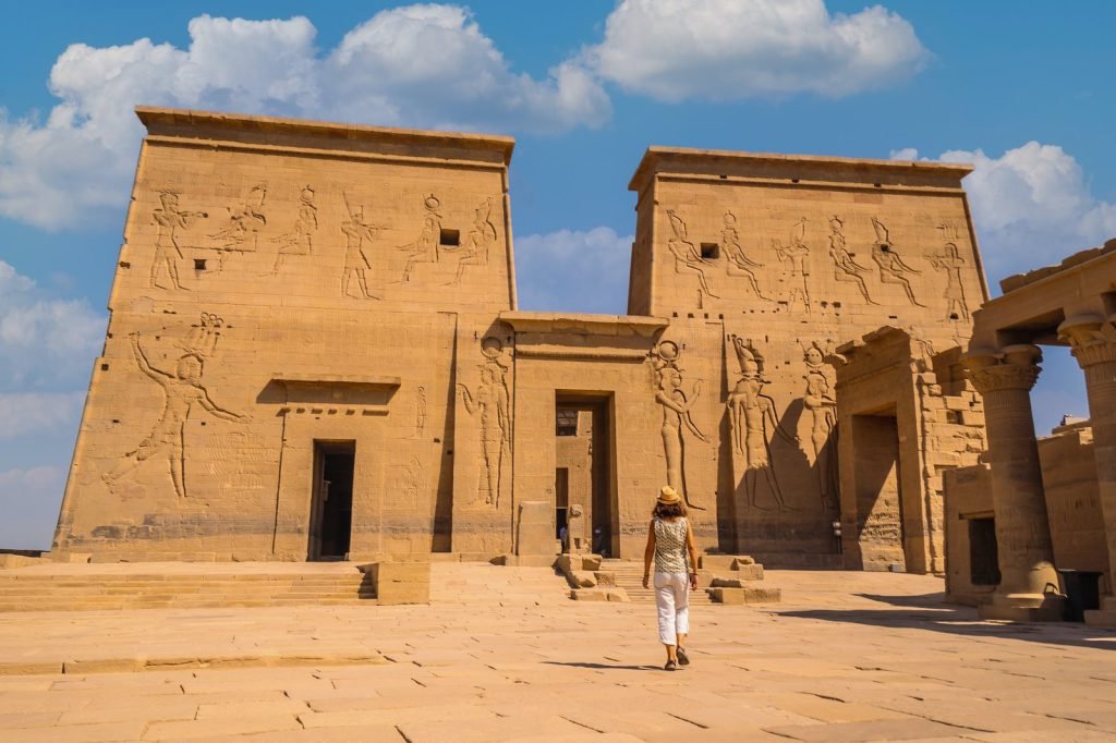 A traveler walking toward the carved first pylon of the Temple of Philae