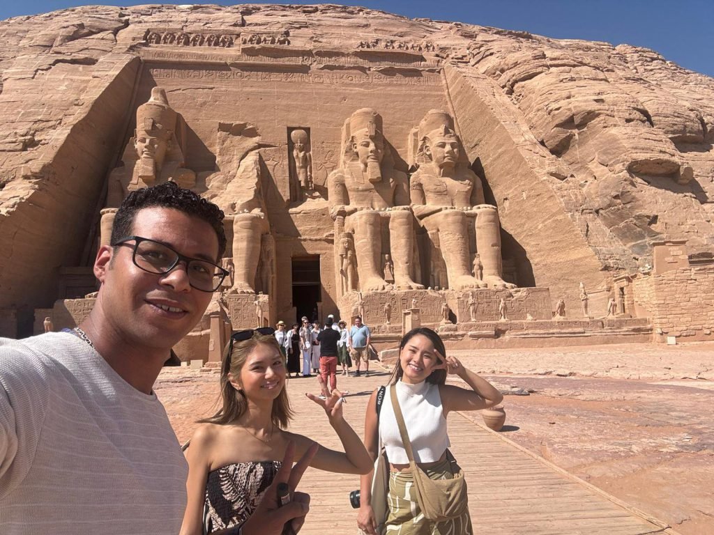 An Amwaj Tour guide taking a selfie with two travelers in front of the Great Temple of Abu Simbel