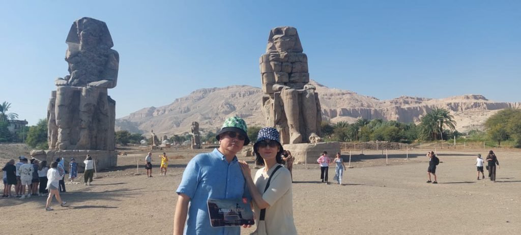 A couple taking a selfie with the Colossi of Memnon behind them