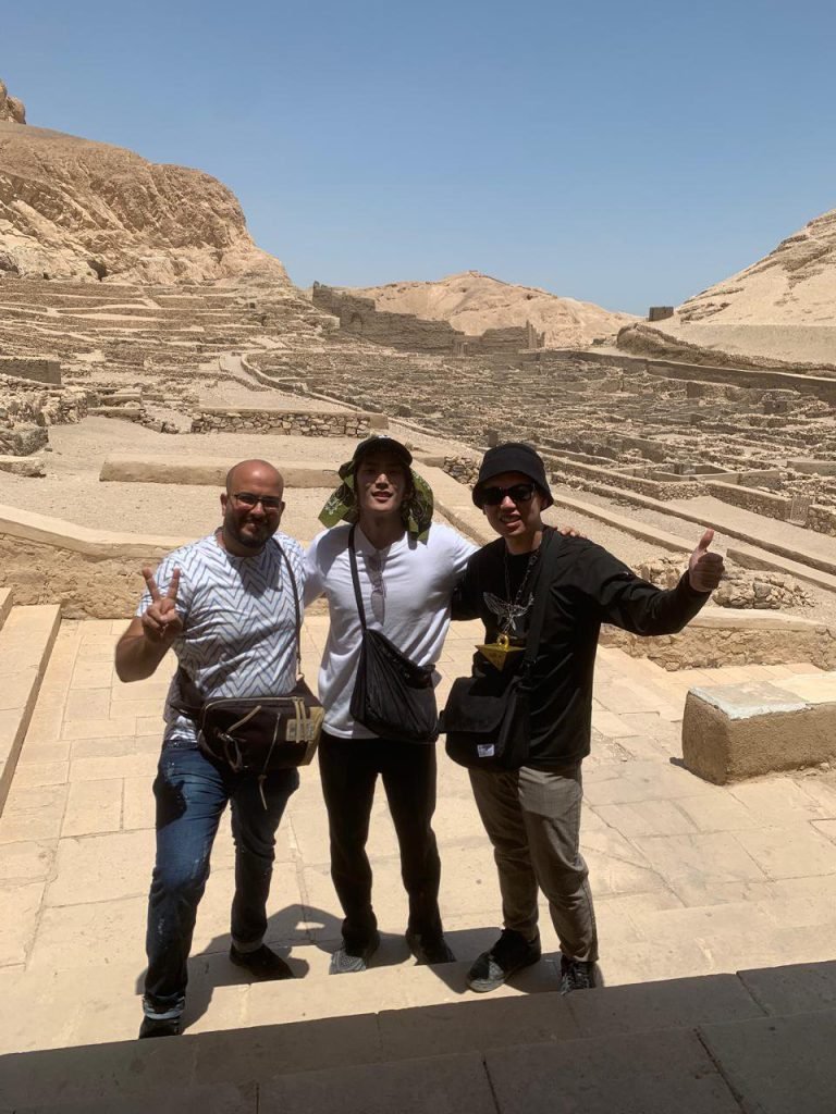 An Amwaj Tour guide with two travelers on a terrace of the Temple of Hatshepsut, with the ruins of Deir el-Bahari behind