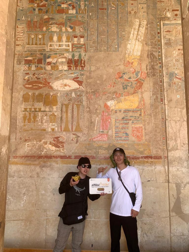 Two travelers beside a brightly painted wall of offerings in the Temple of Hatshepsut