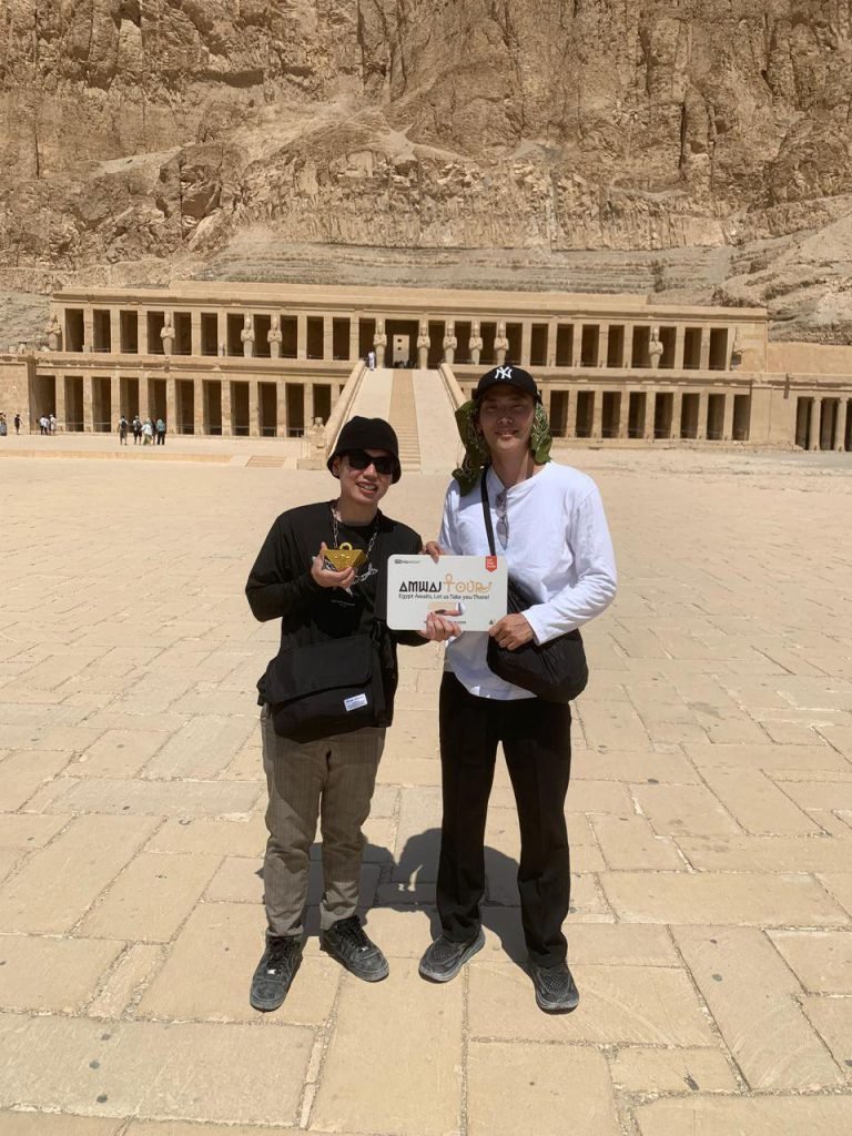 Two travelers holding an Amwaj Tour sign on the forecourt of the Temple of Hatshepsut