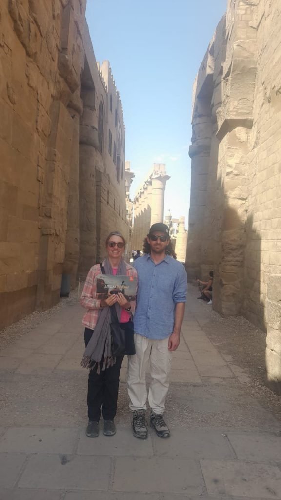 A couple standing in a narrow stone passage at Karnak Temple with an obelisk behind them