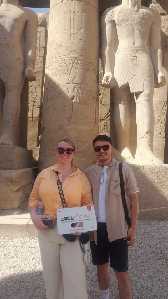 A couple with an Amwaj Tour sign beside the royal statues of Karnak Temple