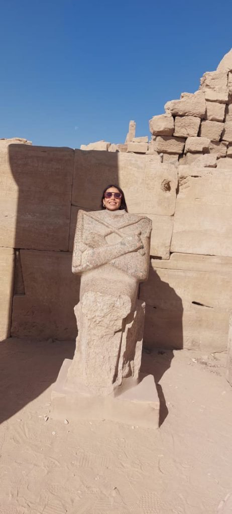 A traveler peeking out behind an ancient Osiris statue in a Luxor temple