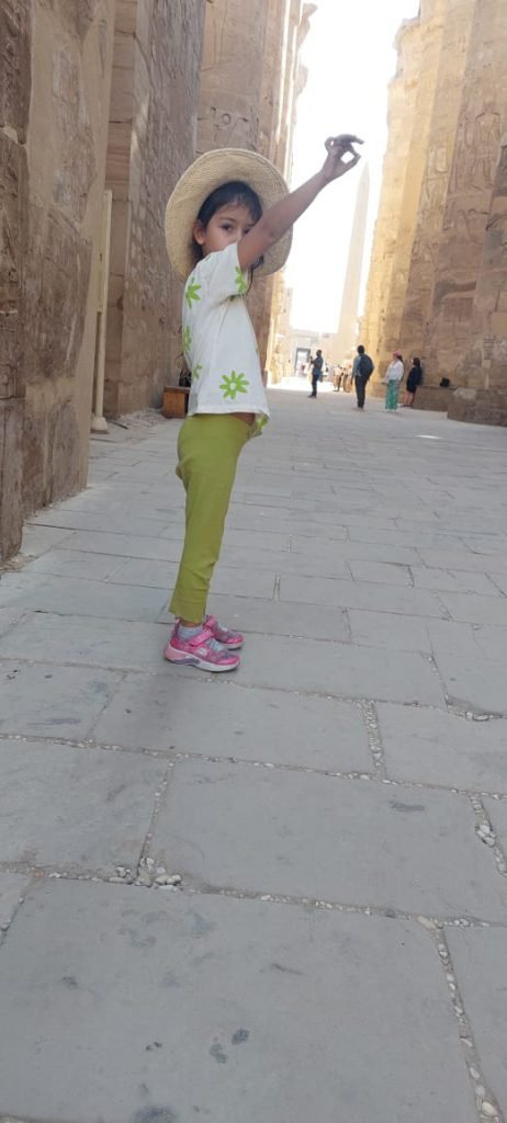 A young girl posing in a stone passage of Karnak Temple, pointing to the sky