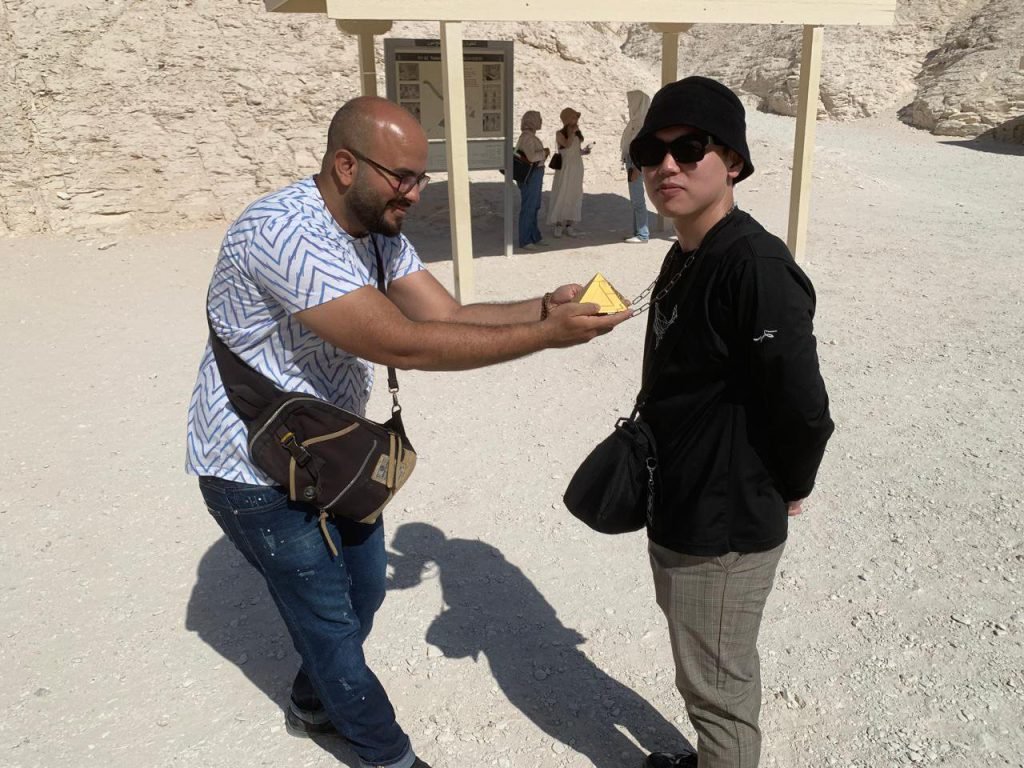 An Amwaj Tour guide giving a small golden pyramid gift to a traveler in the Valley of the Kings