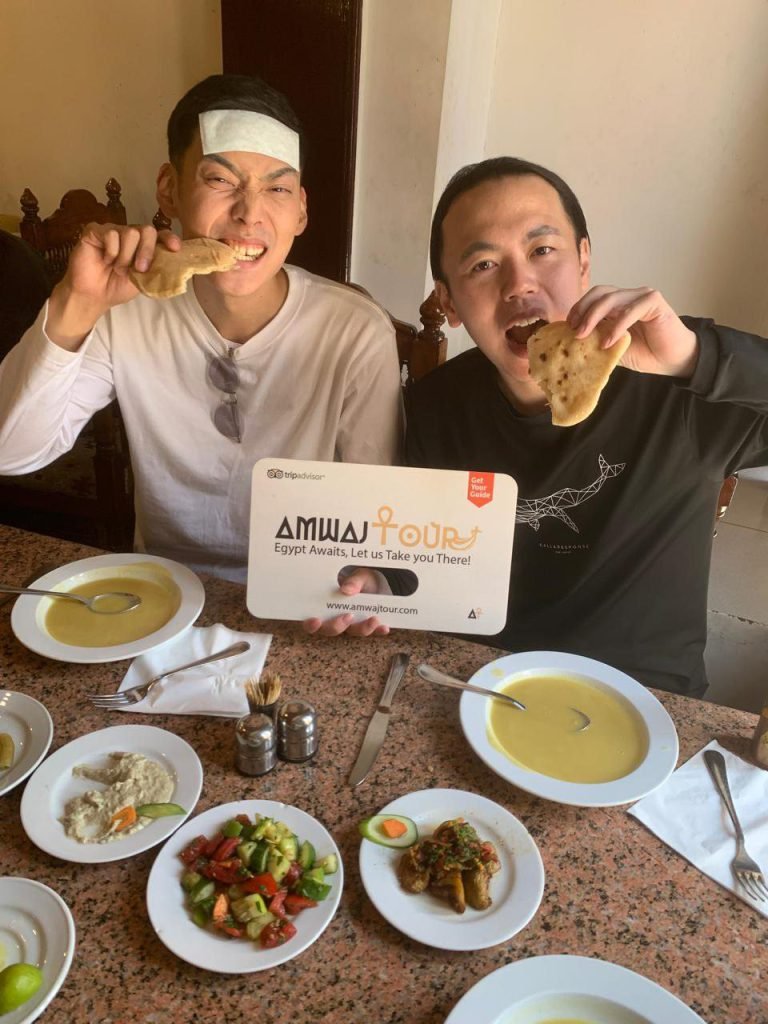 Two travelers with an Amwaj Tour sign enjoying Egyptian bread, lentil soup and salads at lunch