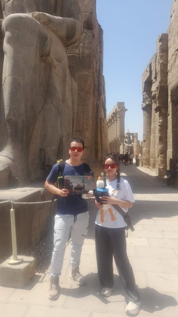 A couple with an Amwaj Tour photo card in the colonnade of Luxor Temple