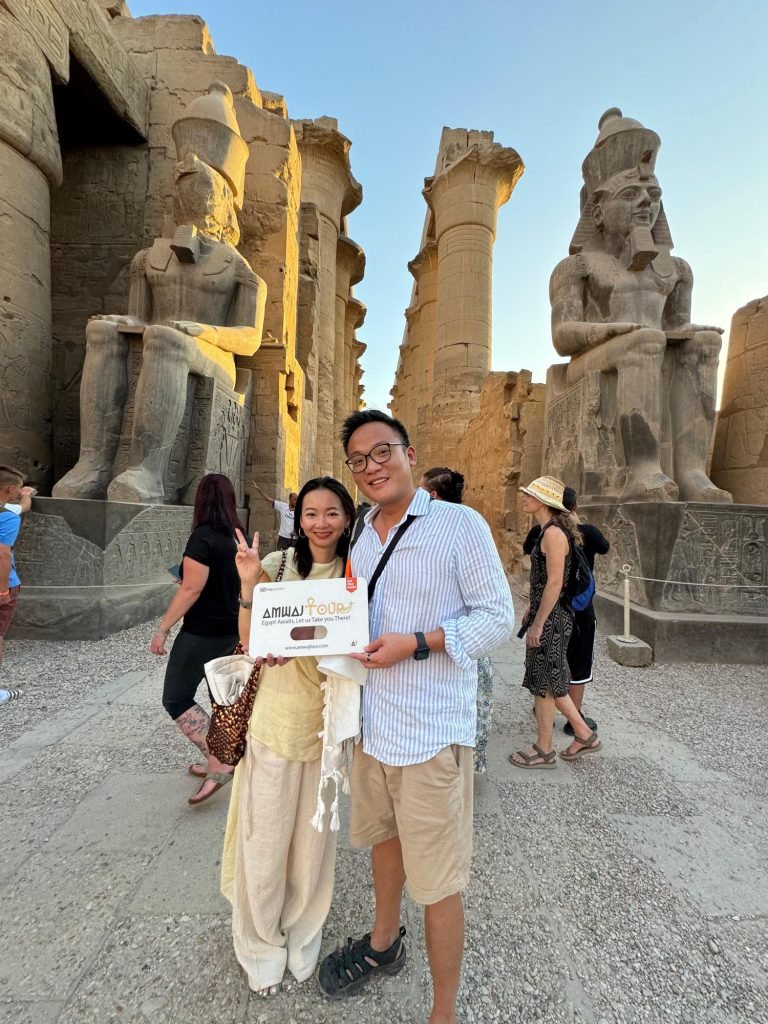 A couple with an Amwaj Tour sign before the statues of Ramses II at Luxor Temple