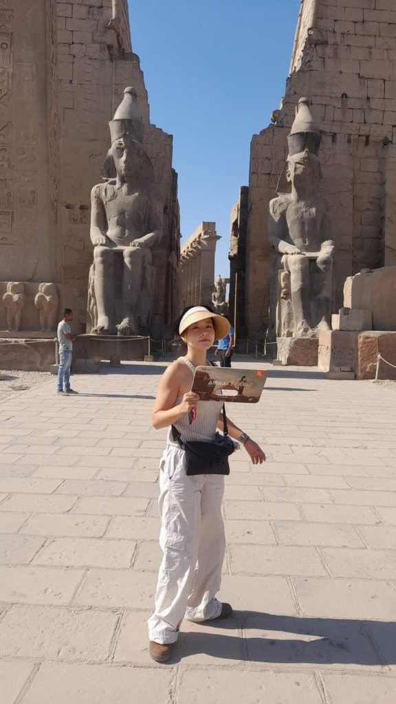 A traveler posing in front of the pylon and statues of Ramses II at Luxor Temple
