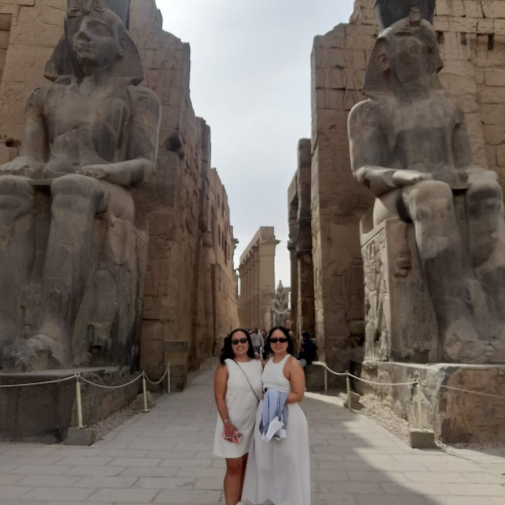 Two travelers in white in front of the seated statues at the entrance of Luxor Temple
