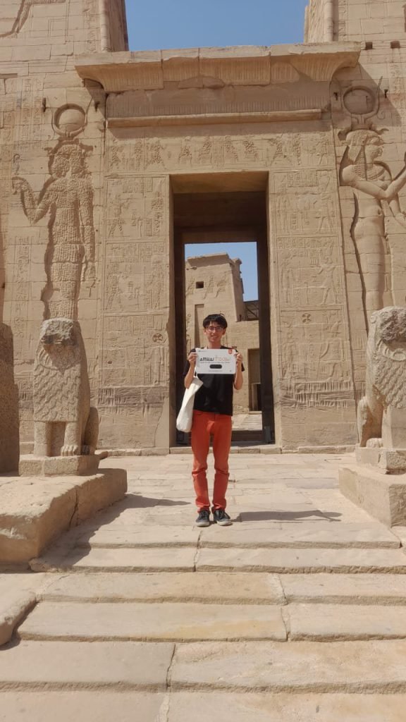 A traveler holding an Amwaj Tour sign in a carved temple gateway at Philae